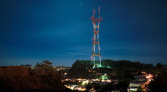 Sutro Tower fasadbelyst på natten. Mörkblå himmel och gatlysen.