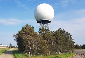 Låg mast med vit boll på toppen omgiven av låga tallar